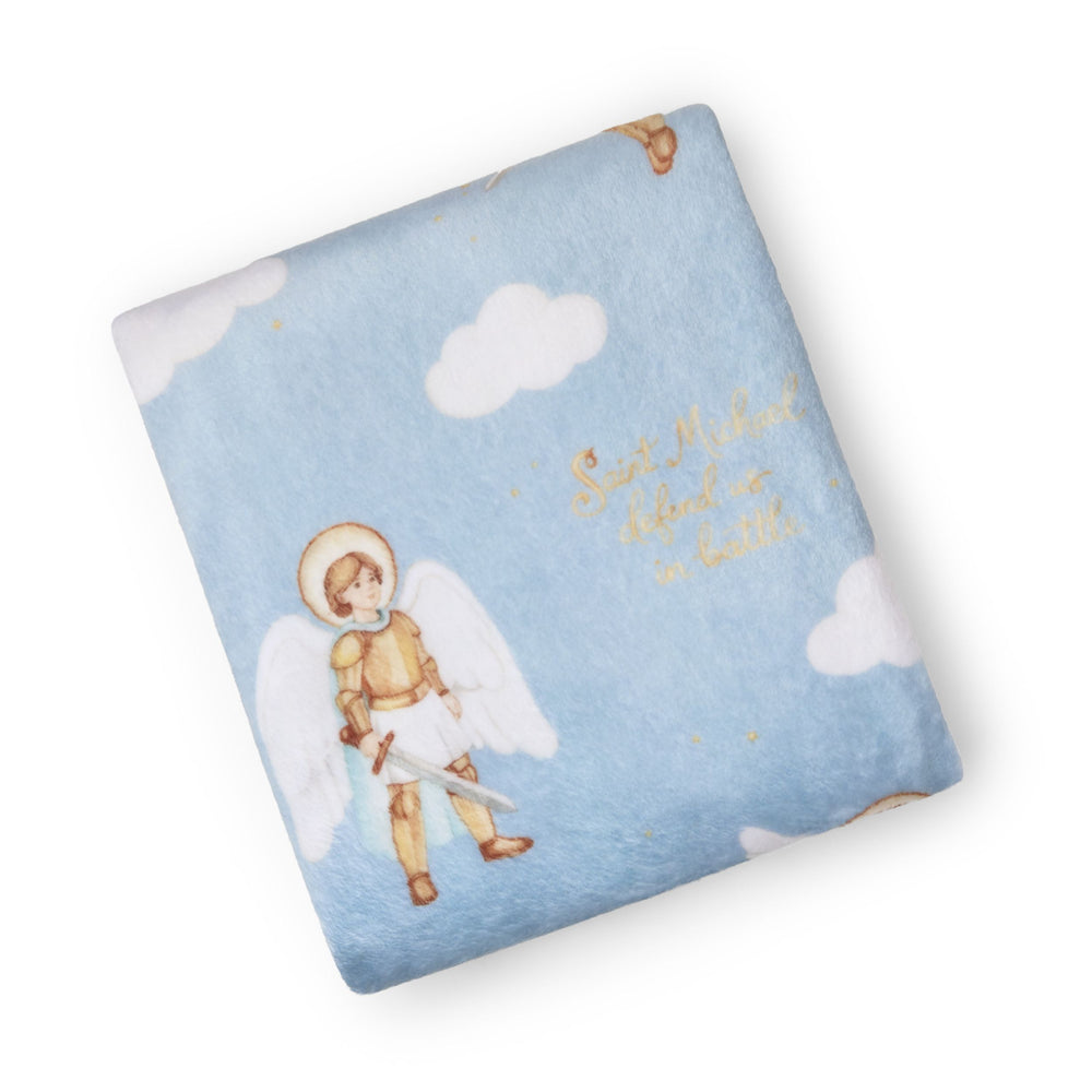 A folded baby blanket featuring a light blue sky design with white clouds, a watercolor-style angel warrior, and gold script text reading 'Saint Michael stood a battle.' on a white background.